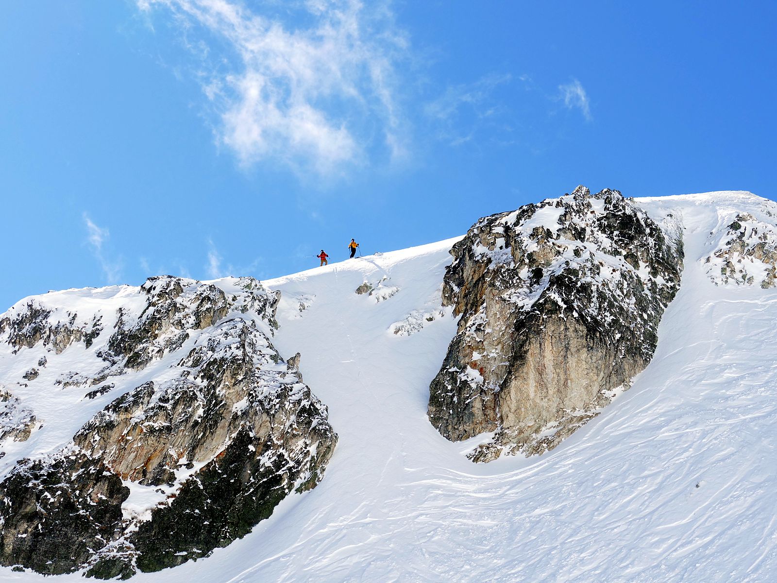Ski tourers on a summit ridge above a couloir in the Valais